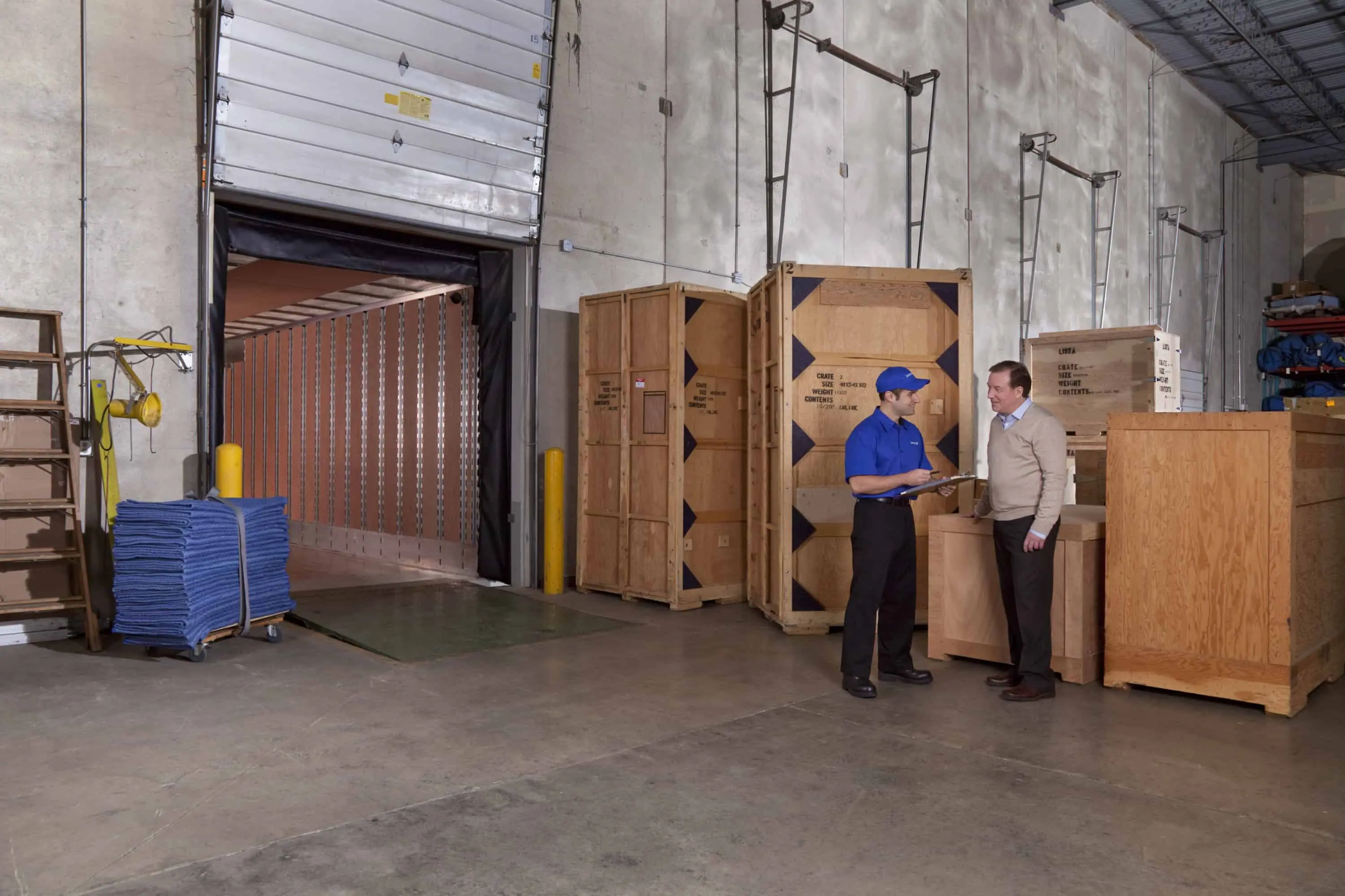 Logistics Company - United worker speaking to a customer in a warehouse with crates and a loading door in the background- United Van Lines